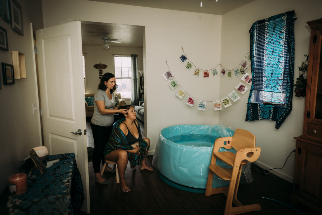 A cozy and inviting birth space with soft lighting and comfortable furnishings for a home birth. Midwife supporting mother near birth tub.