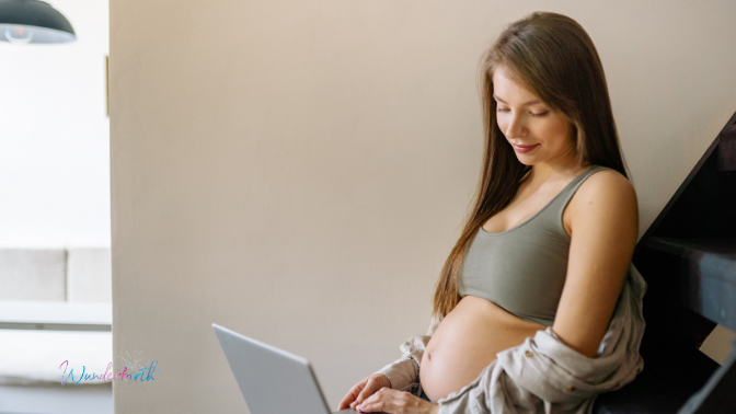 A pregnant woman looking down at her laptop as she choosing the right midwife for her birthing experience.